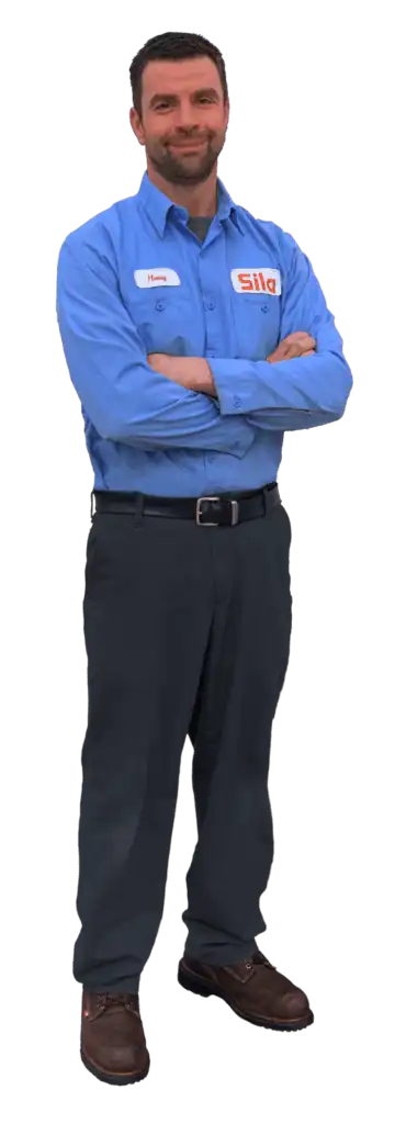 A man in a blue button-up shirt with the "Sila" logo, dark pants, and brown work shoes stands with arms crossed, facing forward.