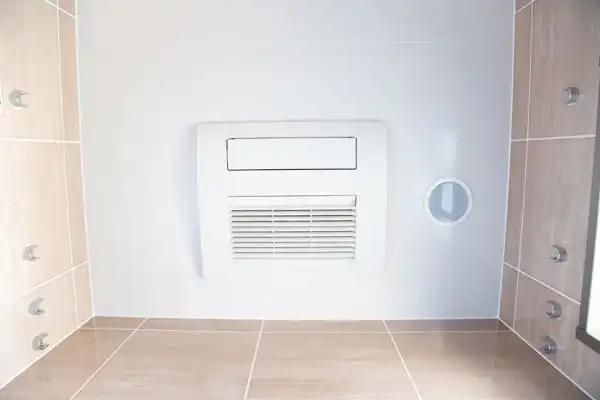 White ceiling-mounted ventilation fan installed in a tiled room in Boston, MA, viewed from below. Perfect addition for improved airflow or as part of a dehumidifier installation. Round duct opening is visible to the right of the fan.
