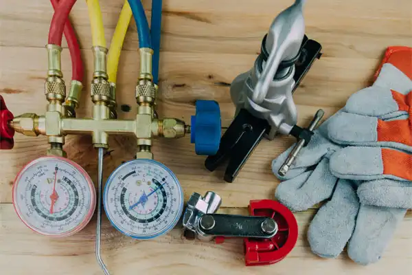 Assorted HVAC tools on a wooden surface, including gauges with colored hoses, a pipe cutter, a hand tool, a valve, and work gloves—perfect for any General Heating Installation or Heating Installation MA project.