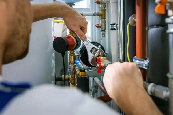 A person in Boston, MA uses a wrench to adjust piping and valves on a plumbing or heating system, possibly preparing for a humidifier installation, surrounded by various pipes and fittings.