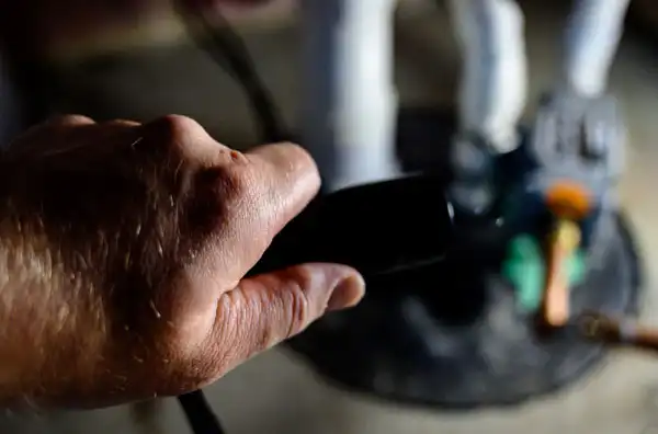 A close-up of a person's hand holding a black object, with blurred white figurines and a round black base in the background—captured during a Sump Pump Installation in Boston, MA.