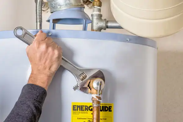 A person in Boston uses a large adjustable wrench to tighten a pipe on a water heater, which has an EnergyGuide label on the front, demonstrating expert Water Heater Repair.