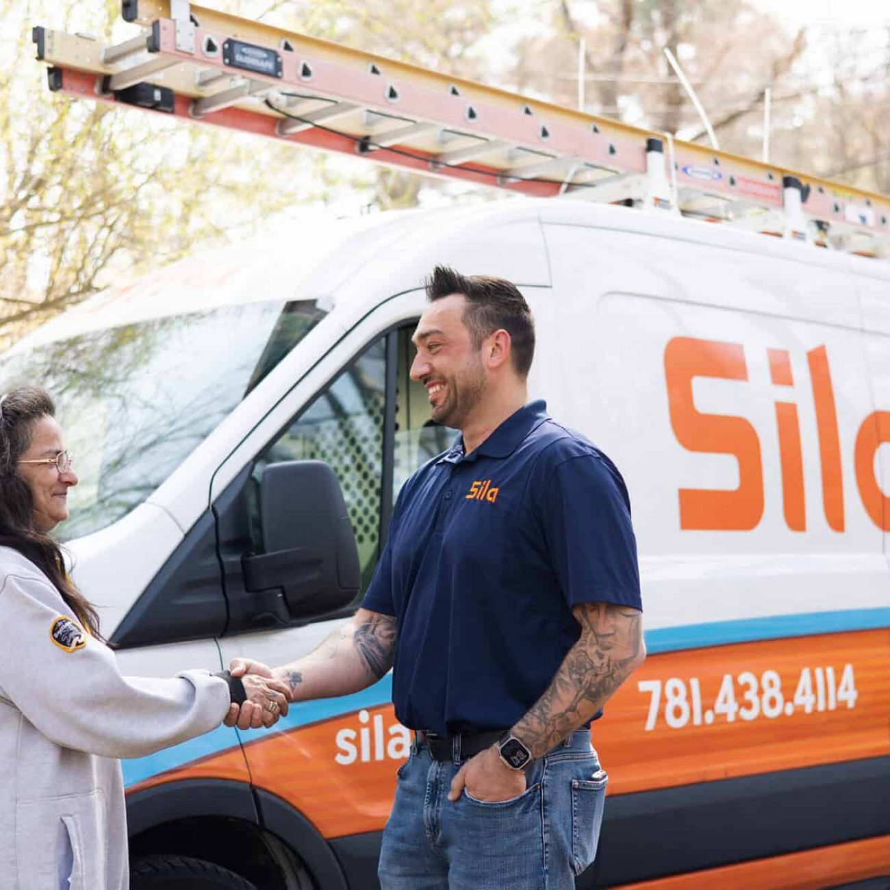 A service technician in a Sila uniform shakes hands with a woman in front of a Sila company van labeled "Heating, Cooling, Plumbing, Electrical.